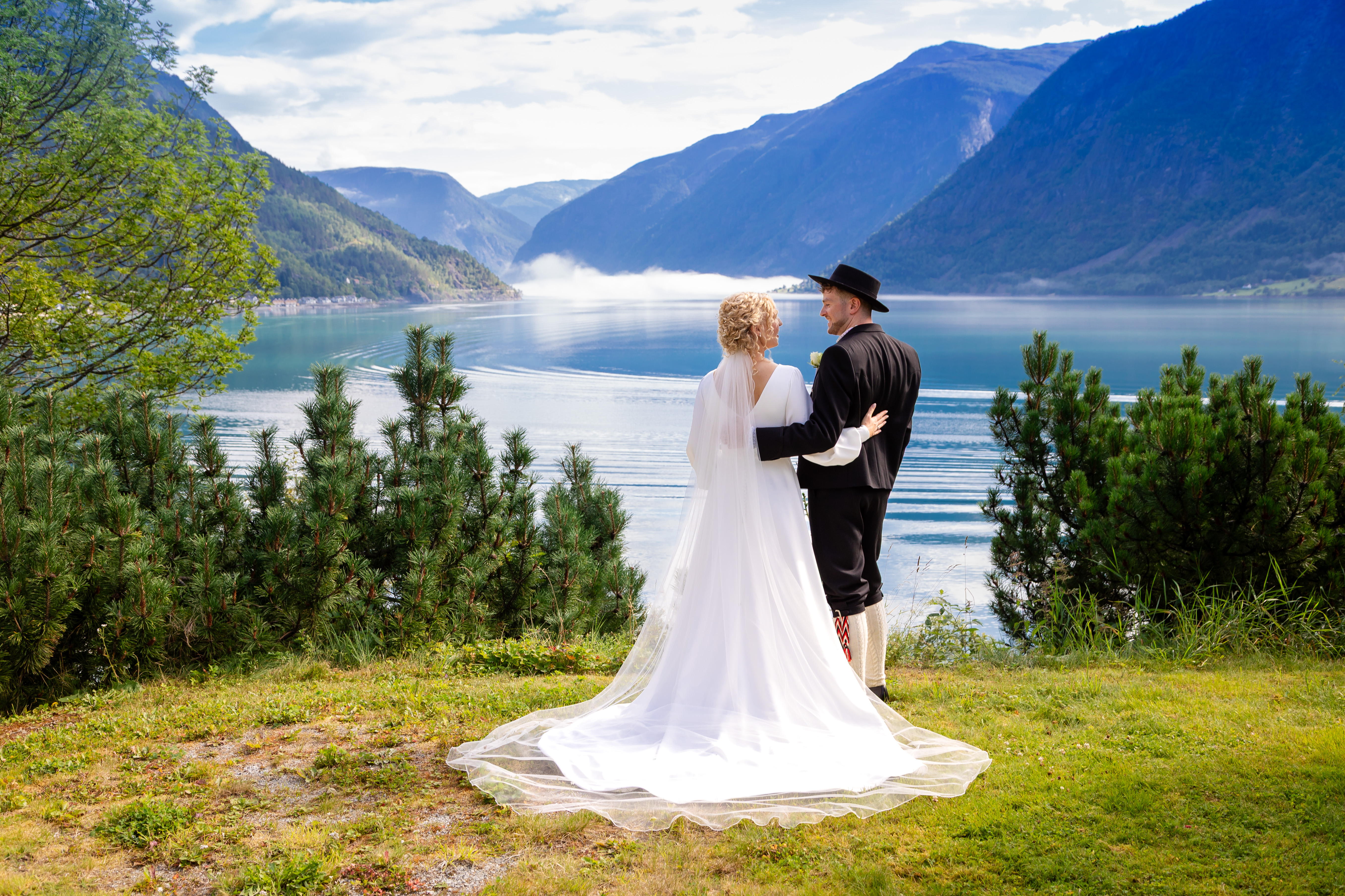 Et lykkelig par holder rundt hverandre, med en fjord og fjell i bakgrunnen.